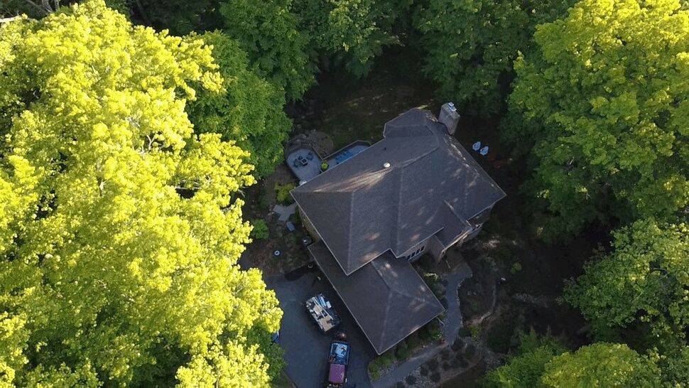 Tree-Lined Roof Inspection | Wells Home Improvements Drone view of a residential roof and landscaped property in a wooded setting.