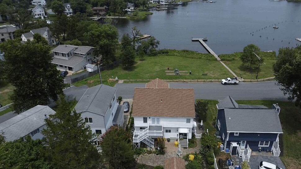 Aerial of a house roof, backyard deck, and nearby waterfront dock.