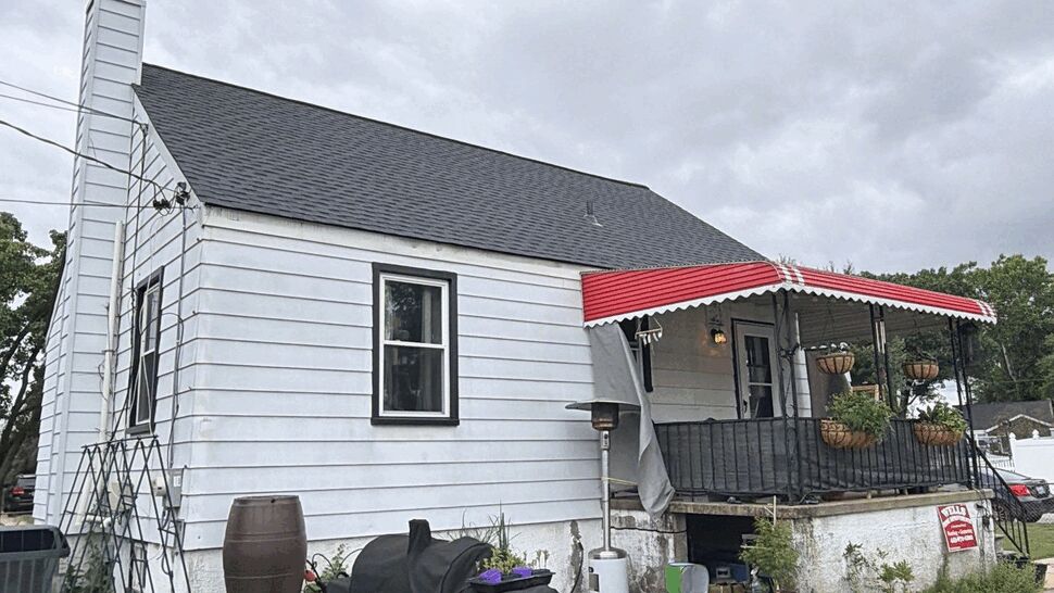 Small white house side porch with red-striped awning, hanging planters, and lawn