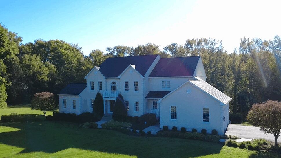 White Home Front Roofing | Wells Home Improvements Front view of a white home with dark roofing, landscaping, and a broad lawn.