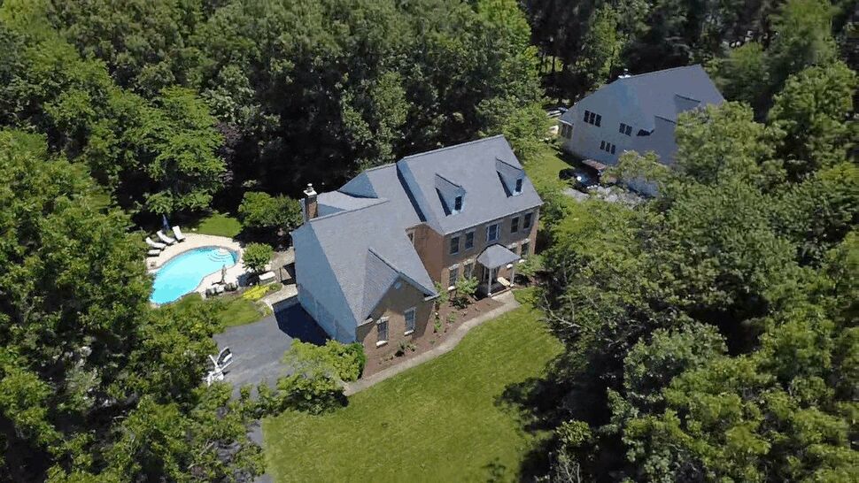 Aerial view of a gray-roofed brick home surrounded by trees and lawn